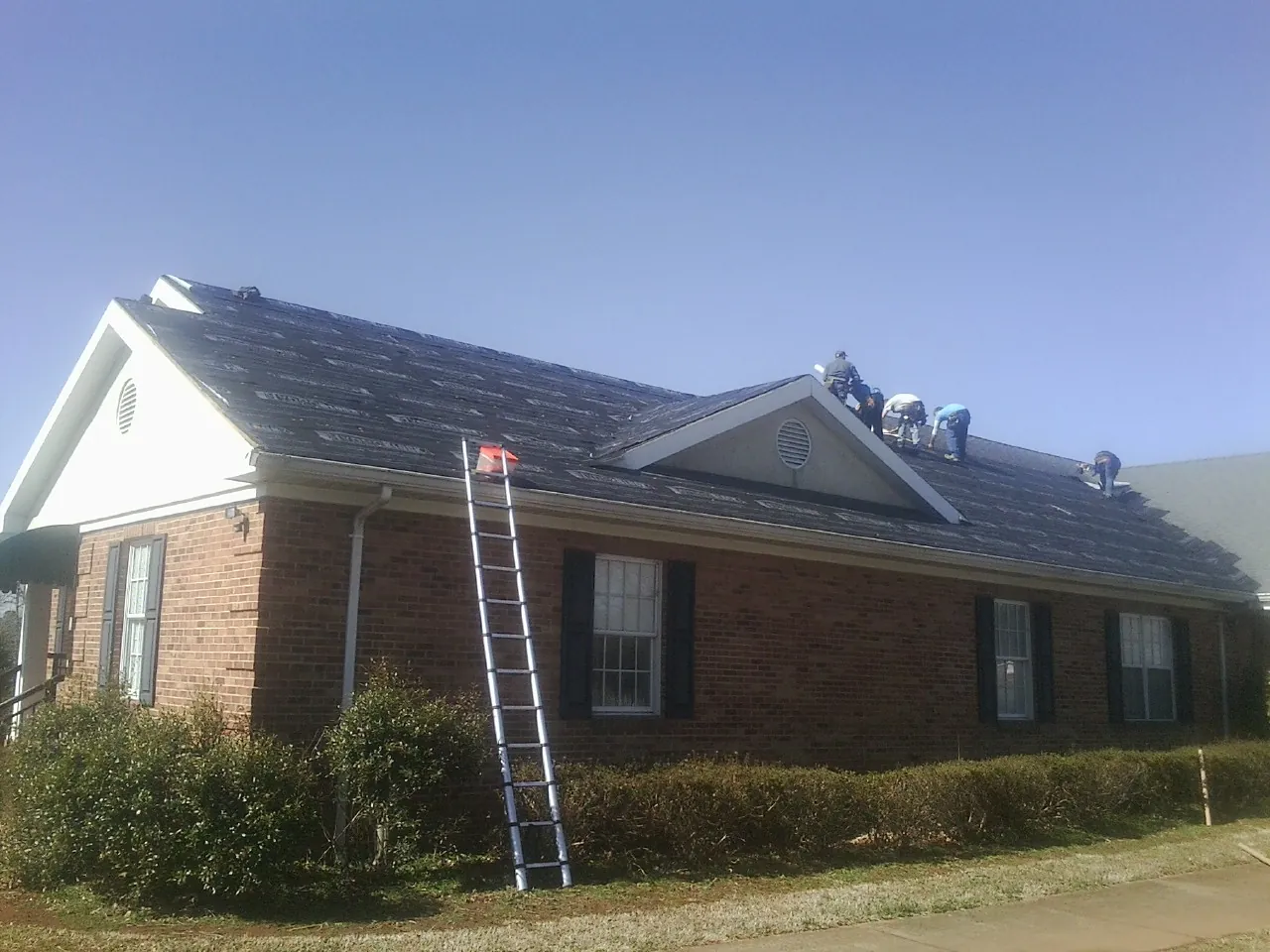 Crew tearing shingles off a brick ranch roof with a ladder set — Emergency Roof Repair work by our crew in Gable