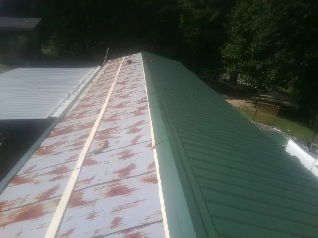 Old rusted panels beside newly installed green metal roofing — Wind Damage Roof Repair by Roofing Brothers in Gable