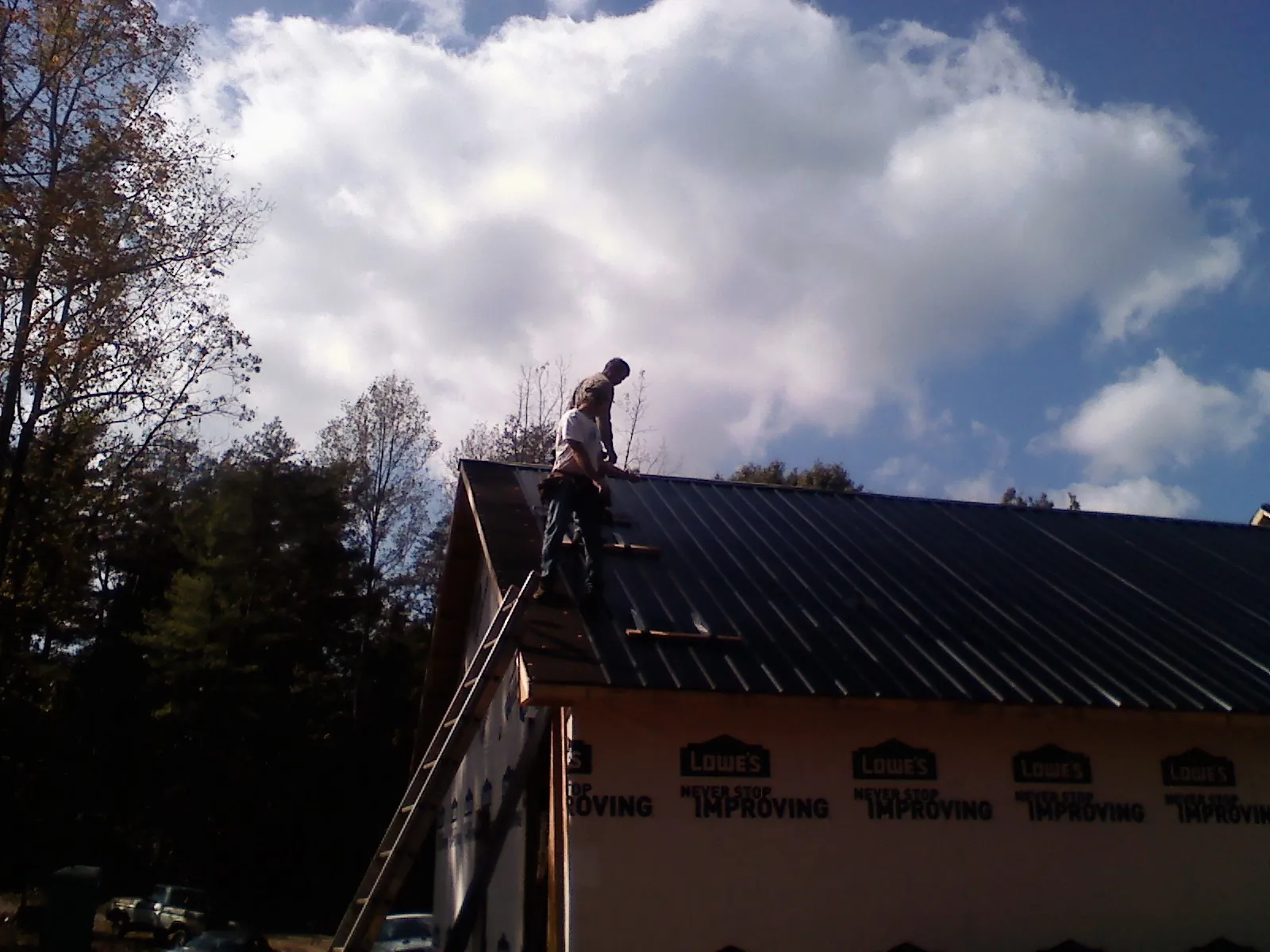 Roofer fastening dark metal panels high against a cloudy sky, from a Roof Inspection job in Gable