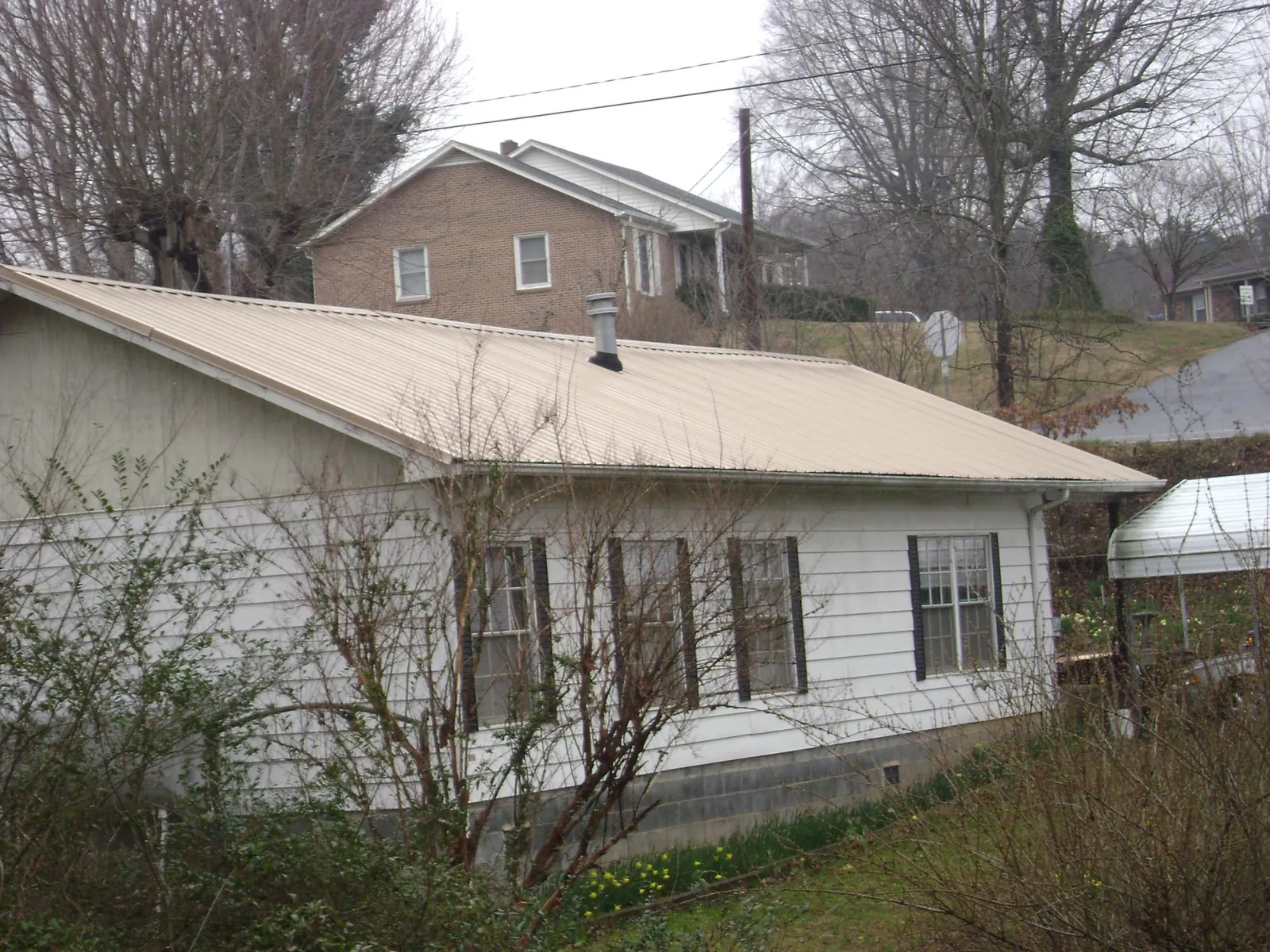 Tan metal roof on a white sided house set into a hillside — Commercial Roofing by Roofing Brothers in Gable